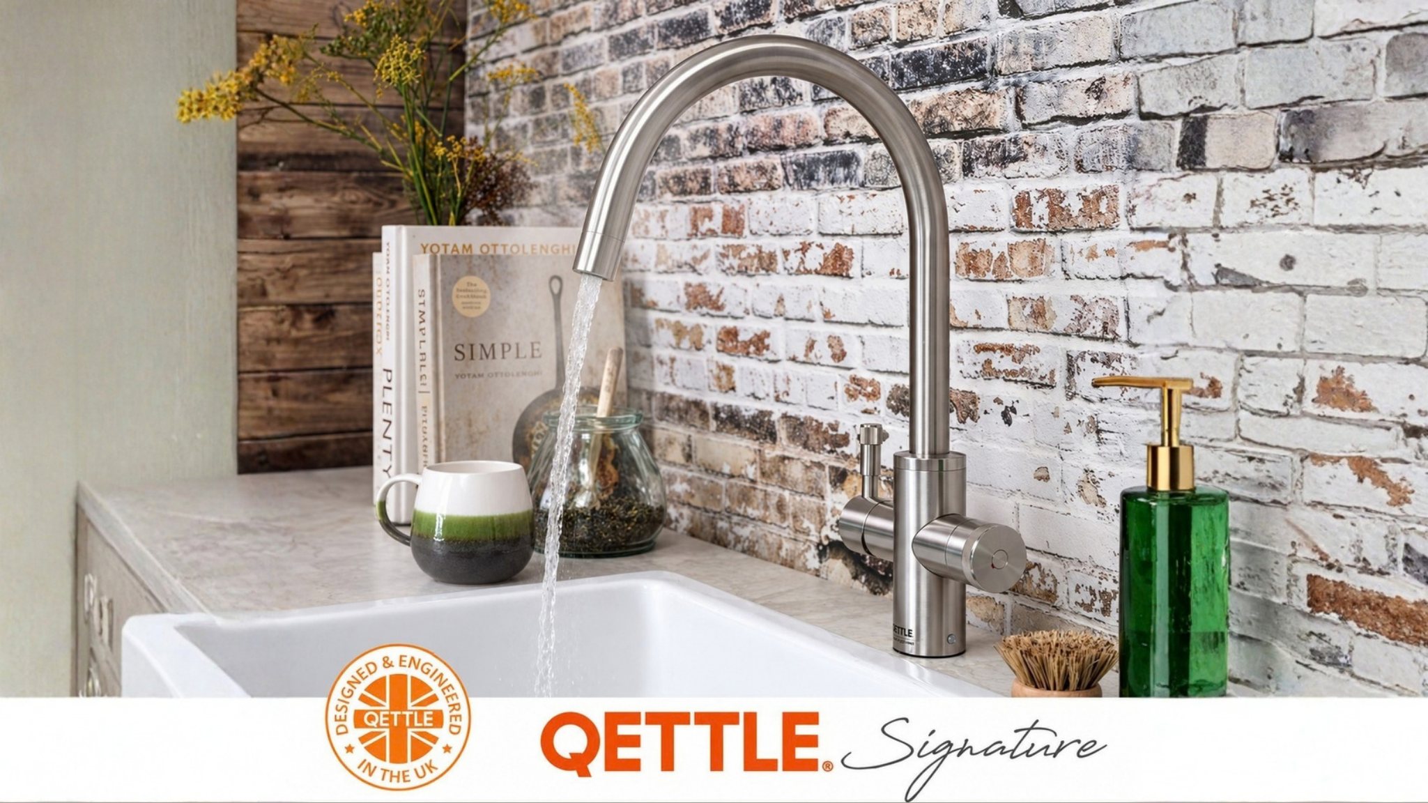 A brushed steel QETTLE boiling water tap over a white ceramic sink, against a painted brick wall. QETTLE Signature, designed and engineered in the UK